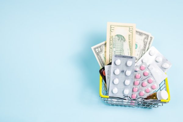 A shopping basket filled with various medications and cash, symbolizing healthcare expenses.